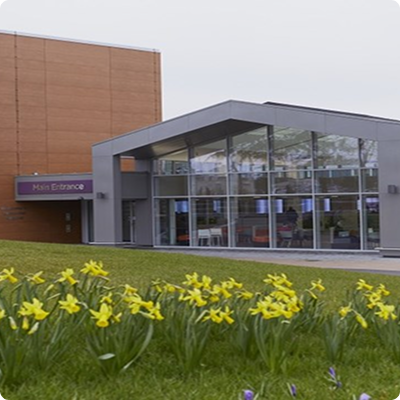 The entrance of the clinic showing a daffodils in bloom outside with modern grey sloping roof and big windows covering the front of the building.